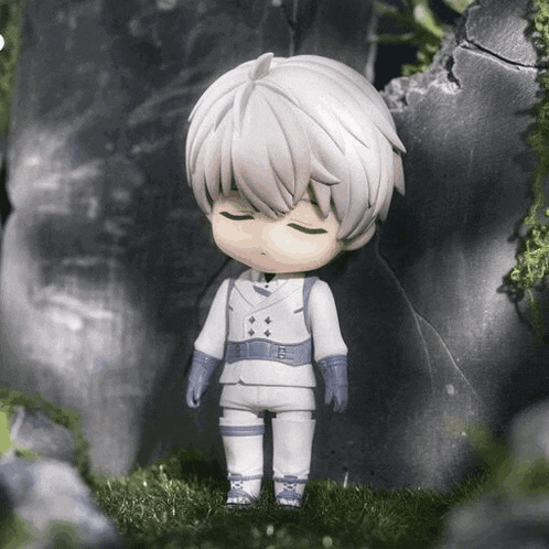 a figurine of a boy with white hair and blue gloves is standing in the grass .
