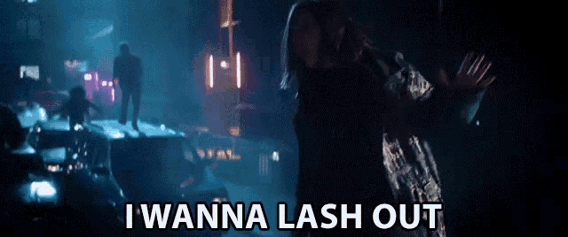 a woman is dancing in a dark room with the words i wanna lash out behind her