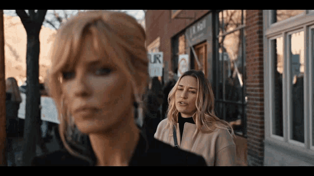 two women are standing in front of a building with a sign that says our