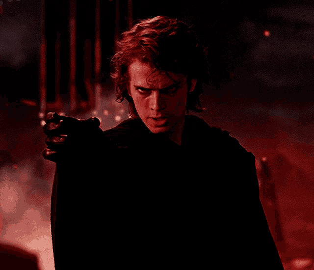 a man in a black cape is holding a gun in a dark room