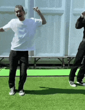 a man in a white shirt and black pants is dancing on a green grass field .