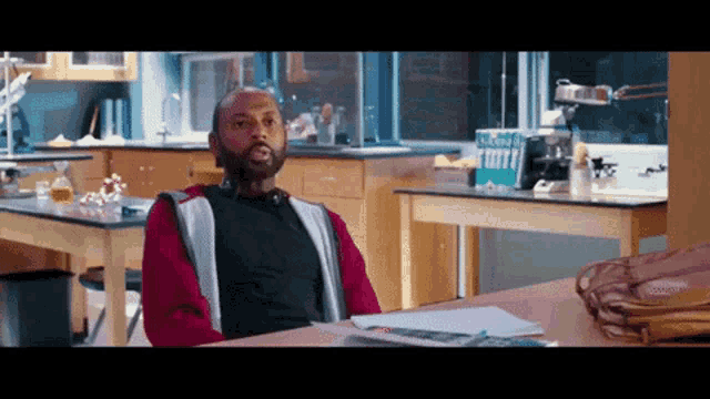 a man sits at a desk in a classroom with a box of kleenex on it