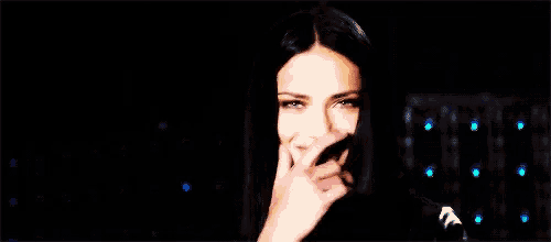 a woman with long black hair is covering her mouth with her hand in a dark room .