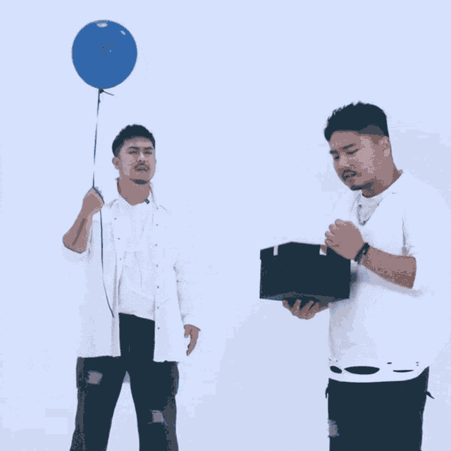 a man holds a blue balloon while another man holds a gift box