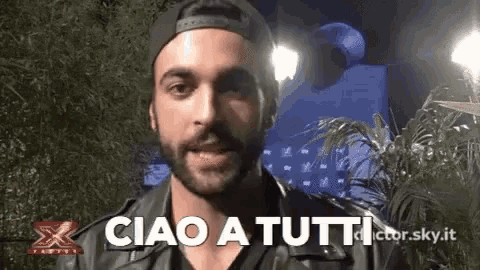 a man with a beard wearing a hat and a leather jacket says ciao a tutti .