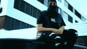 a man wearing a mask sits on top of a black car