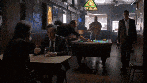 men playing pool in a bar with a stained glass triangle hanging from the ceiling