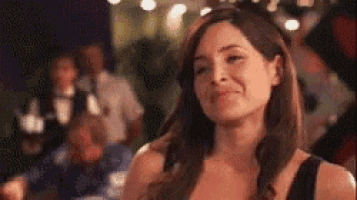 a woman in a black dress is smiling and looking at the camera in a blurry photo .