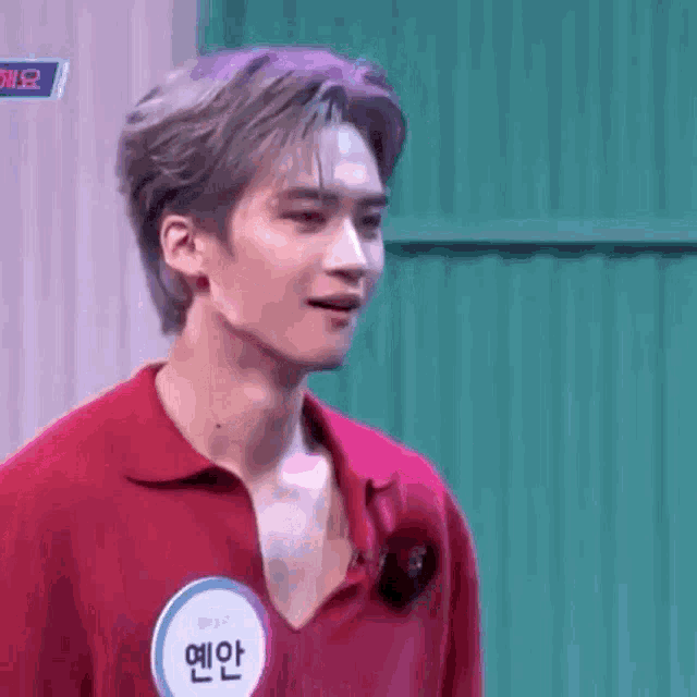 a young man wearing a red shirt with a name tag on his chest is standing in front of a green wall .