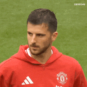 a man wearing a red manchester united hoodie is standing on a soccer field .
