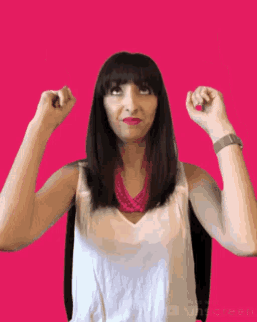 a woman wearing a white tank top and a pink necklace holds her fists up in the air