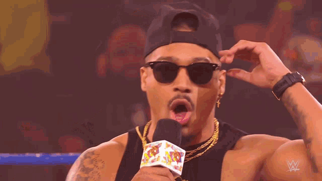 a man wearing sunglasses and a hat is holding a microphone