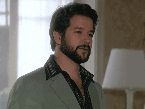 a man with a beard wears a green jacket and black shirt