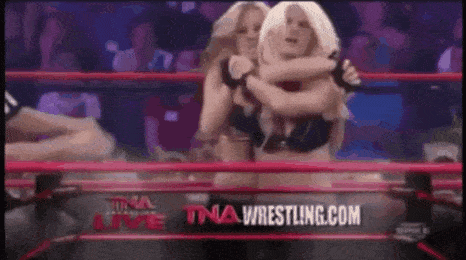 two women are wrestling in a ring with a tna wrestling logo in the background .
