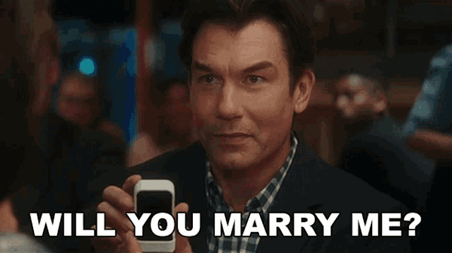 a man holding a cell phone with the words will you marry me above him