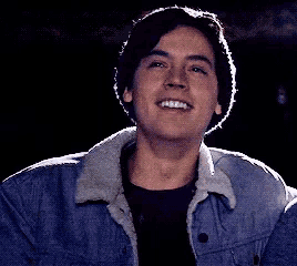 a young man wearing a denim jacket is smiling in a dark room