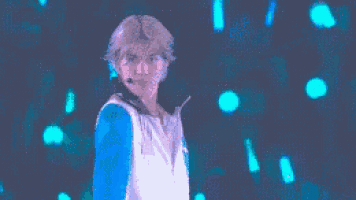 a person in a blue and white shirt is standing in front of a stage with a microphone .