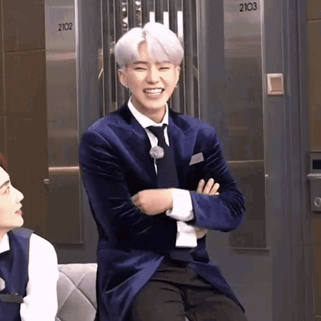 a man in a blue suit and tie is sitting in front of a door that says 2103