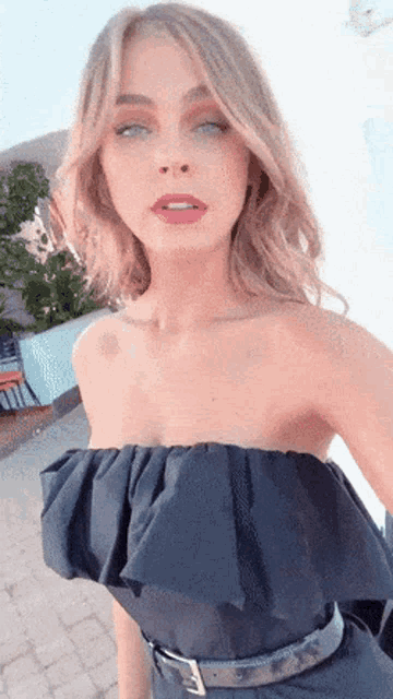 a woman wearing a black strapless top is taking a selfie with her eyes closed