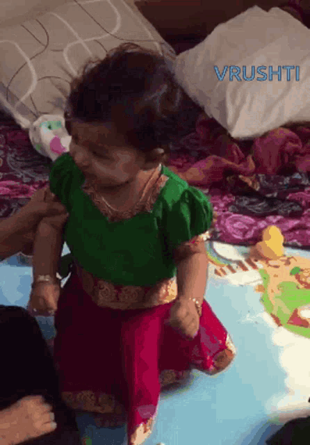 a little girl wearing a green top and a red skirt is sitting on a bed with the word vrusht written on the bottom