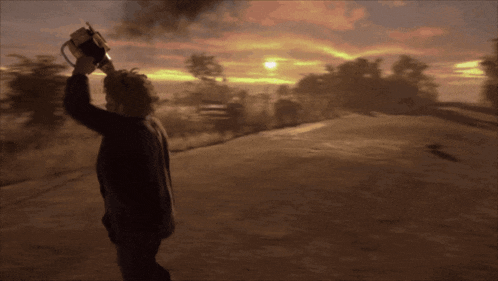 a person holding a chainsaw in front of a sunset sky