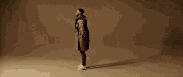 a man in a trench coat and white sneakers is standing in a room