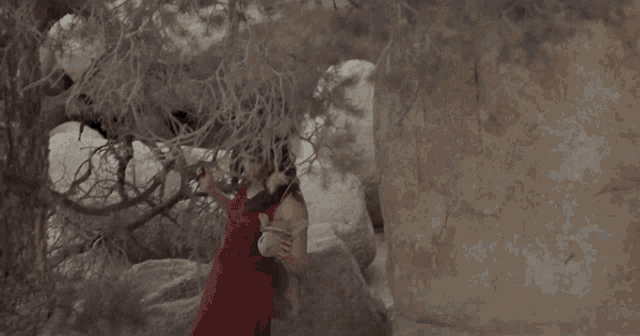 a woman in a red dress is standing next to a rock