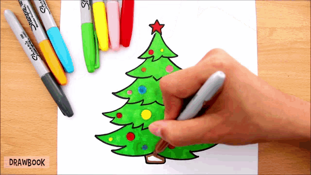 a person is drawing a christmas tree with sharpie markers in the background