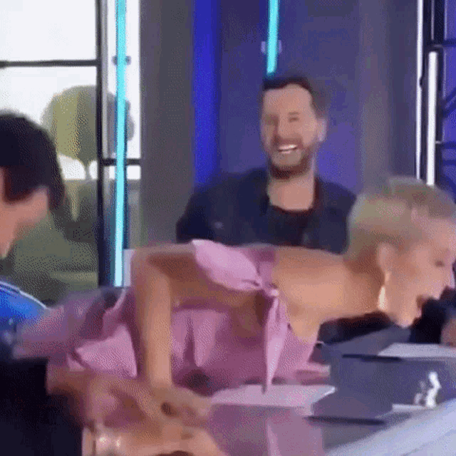 a woman in a pink dress is laughing while sitting at a table with two men .