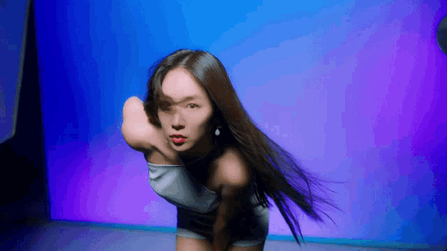 a woman with long hair is dancing in front of a blue and purple wall