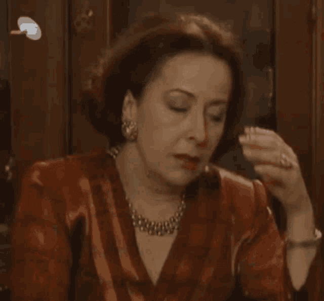 a woman wearing a necklace holds her hand to her head