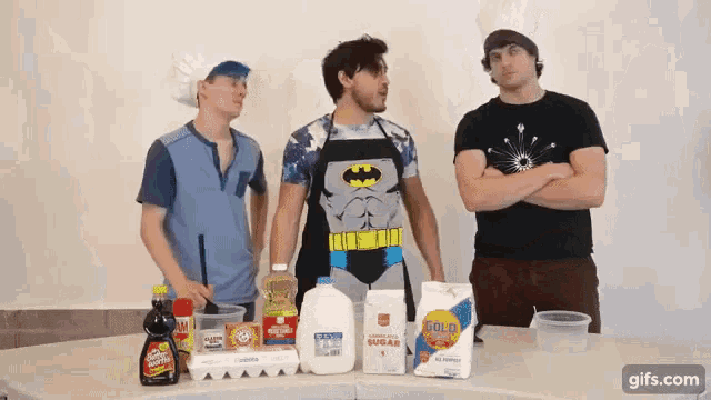 a man in a batman apron stands in front of a table full of food items