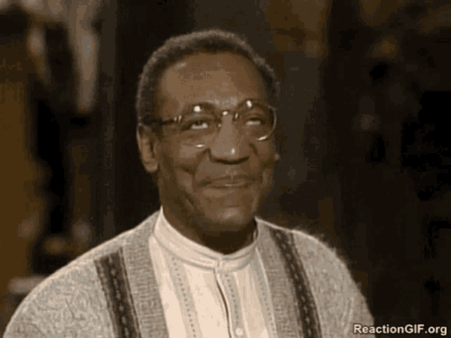a man wearing glasses and a sweater is smiling at the camera .