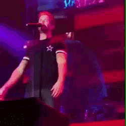 a man singing into a microphone on a stage with a purple background
