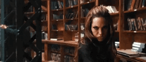 a woman in a black jacket is standing in front of a bookshelf in a library .