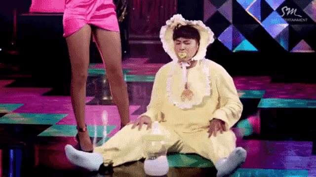 a woman in a pink dress is standing next to a man dressed as a baby with a pacifier in his mouth