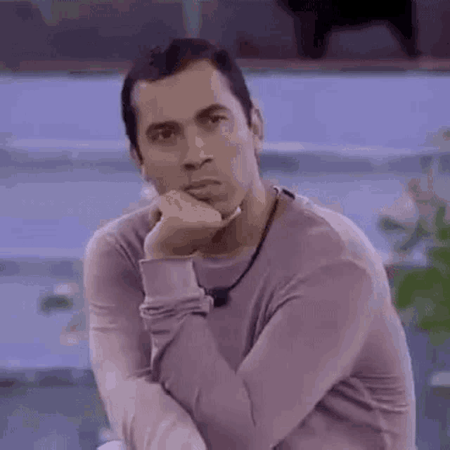 a man in a pink sweater is sitting with his hand on his chin and his eyes closed .