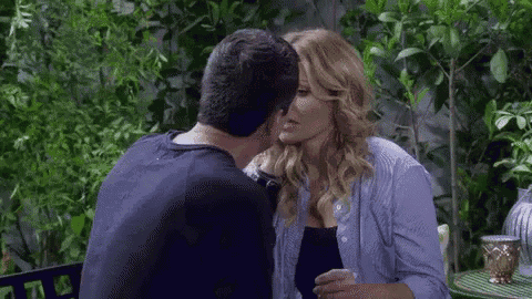 a man and a woman are kissing while sitting at a table in front of trees .