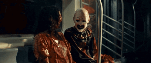 a clown is sitting next to a woman with blood on her face