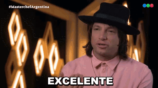 a man wearing a hat and a pink shirt says excelente in front of a neon sign