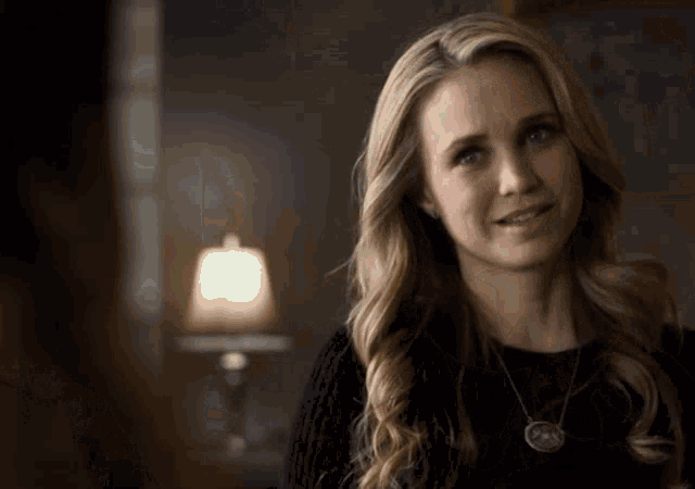 a woman wearing a black sweater and a necklace with a pendant on it