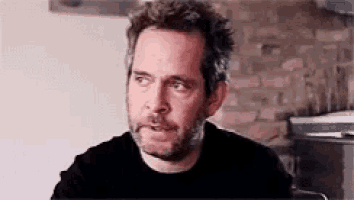 a man with a beard is sitting in a chair in front of a brick wall .