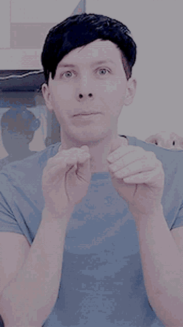 a man in a blue shirt is smiling and making a heart shape with his hands