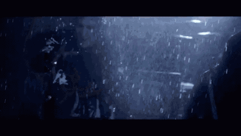 a man is standing in the rain in a dark room with a gun in his hand .