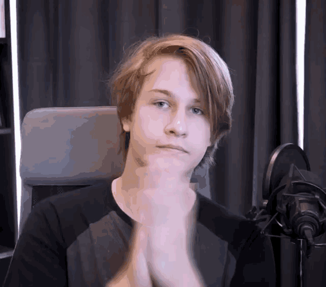 a young man is sitting in front of a microphone with his hands folded
