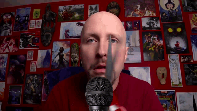 a bald man is holding a microphone in front of a wall with pictures on it including one that says ' marvel '