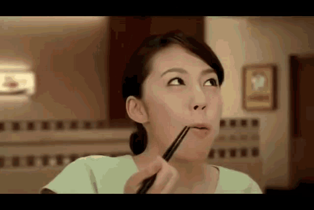 a woman is eating food with chopsticks in a restaurant and making a funny face .