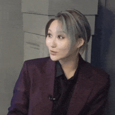 a woman wearing a purple jacket and a black shirt is looking at the camera
