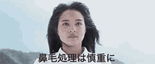 a woman with long hair is wearing a white shirt and looking at the camera with japanese writing on the bottom .