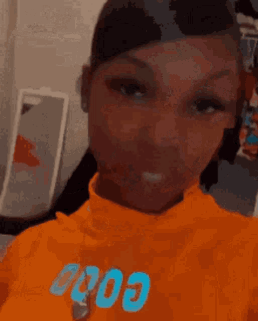 a woman is taking a selfie in a room while wearing an orange sweater .